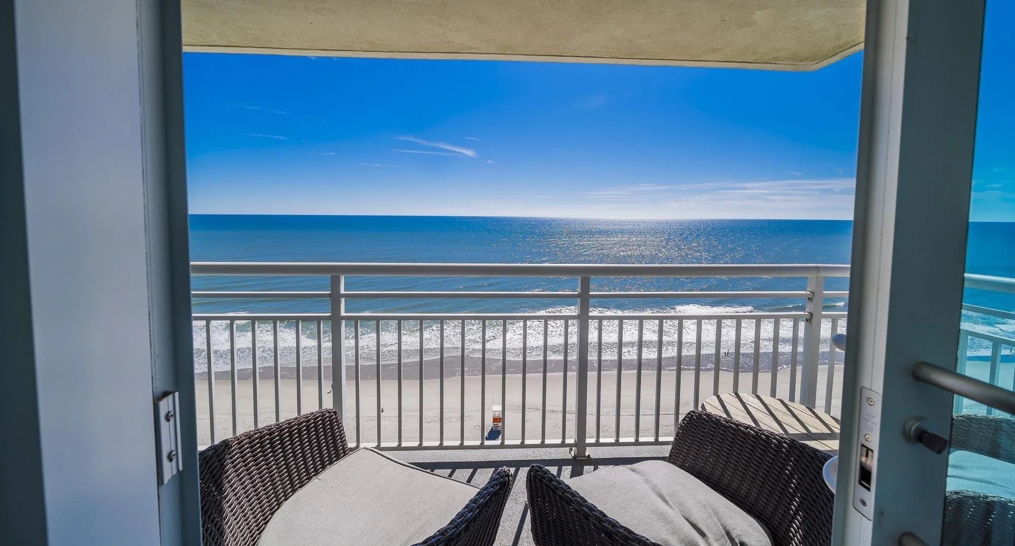 A balcony with wicker furniture and a view of the beach and ocean.