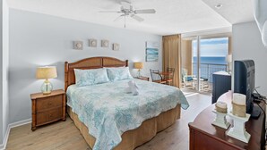 Ett hotellrum med en stor säng, en takfläkt, en balkong med utsikt över havet och en tv-apparat på ett träbord.