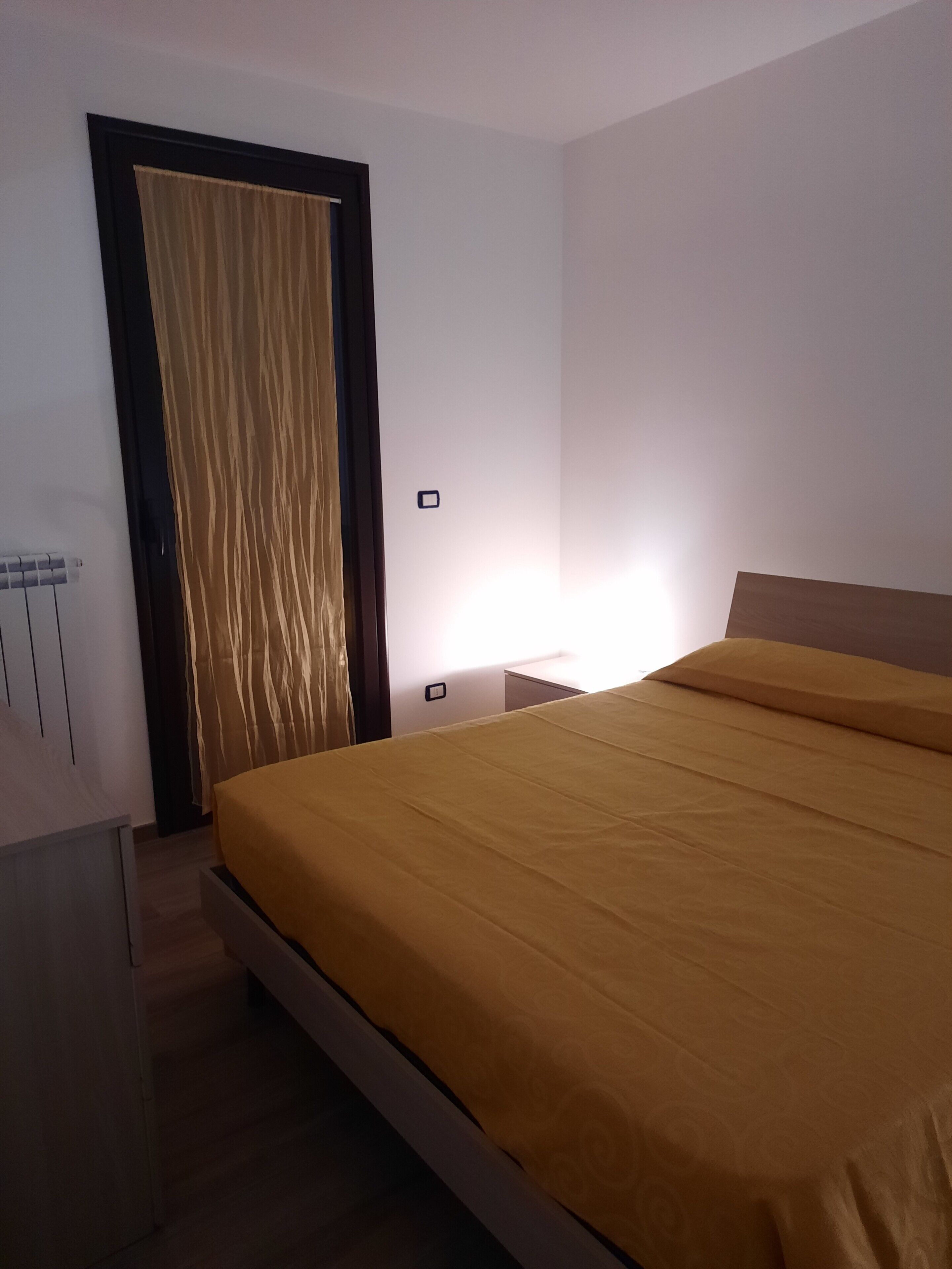 Un dormitorio con cama, mesita de noche, lámpara, armario y una puerta con cortinas.