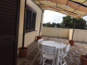 A patio with a white table and chairs, a brown door, and a window with shutters.