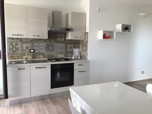 A modern kitchen with white cabinets, a stainless steel range hood, and patterned backsplash tiles.