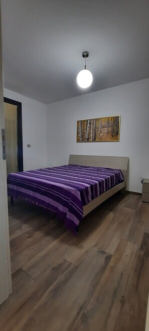 A bedroom with a bed, a painting on the wall, and a ceiling light.