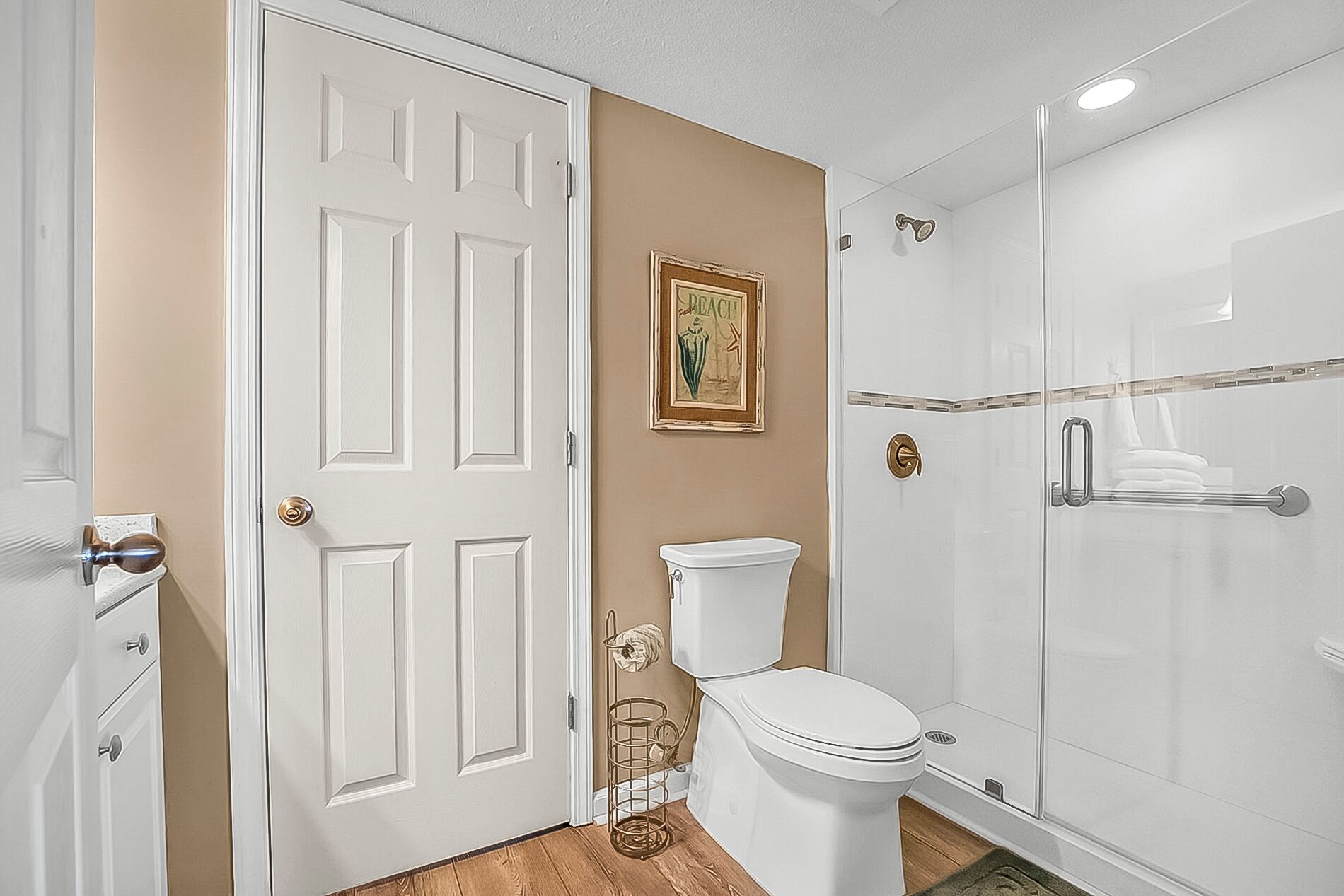 Un bany amb un vàter blanc, una cabina de dutxa de vidre i una paret beix amb un quadre.