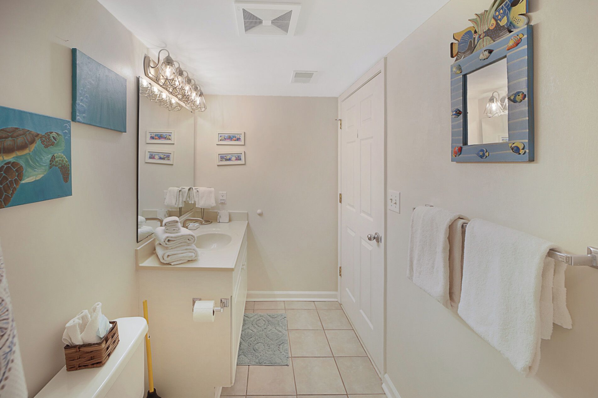 Un baño con lavamanos, espejo, toallero y un espejo decorativo con forma de pez.