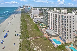 A beachfront hotel with multiple floors, a pool area, and a beach with umbrellas. - WaterPointe II #905-Oceanfront Treasure-Pools,Gym (North Myrtle Beach)