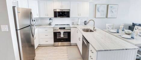 A modern kitchen with white cabinetry, stainless steel appliances, and a marble countertop.
