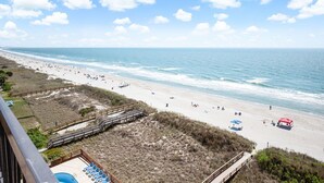 A beach with a wooden boardwalk, a pool area, and beachgoers. - WaterPointe II #905-Oceanfront Treasure-Pools,Gym (North Myrtle Beach)