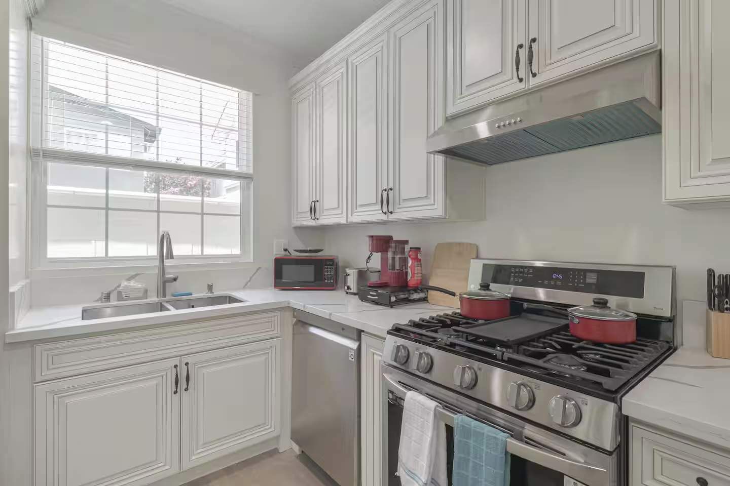 A modern kitchen with white cabinetry, a stainless steel stove, a microwave, and a sink.