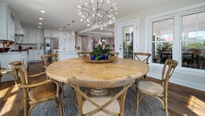 Eine moderne Küche mit weißen Schränken, einer zentralen Kochinsel und einem Essbereich mit Holztisch und Korbstühlen.