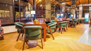 A restaurant with wooden tables and green upholstered chairs, large windows, and a herringbone floor pattern. - Carom Hotel Manali (Manali)