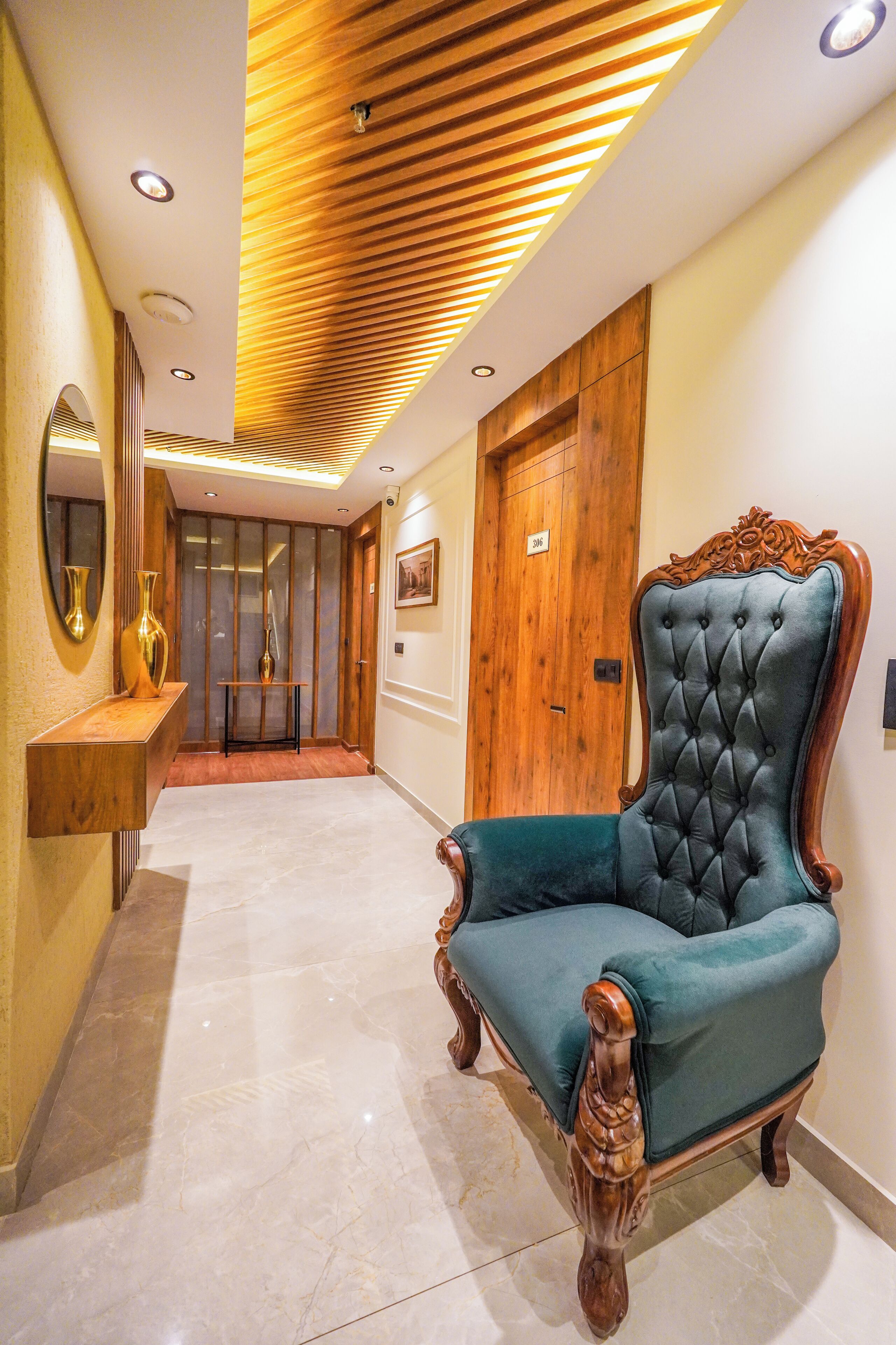A hallway with a wooden ceiling, a blue upholstered chair, a wooden door, and a mirror on the left wall.