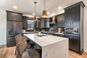 A modern kitchen with dark cabinetry, a marble island, and pendant lighting. - Luxury Townhome-Fireplace-Private Patio w/Firepit (Sevierville)