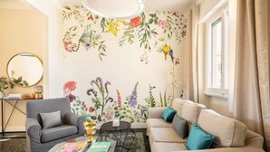 A living room with a floral wall mural, a grey sofa, a beige sofa, a round coffee table, and a side table with books and a lamp. - Bright penthouse apartment for friends and families (Firenze)