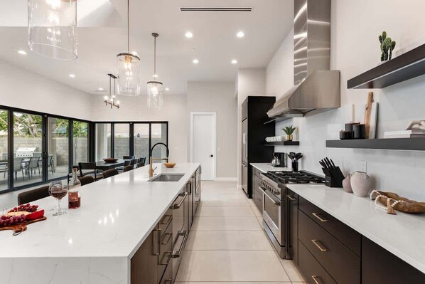 A modern kitchen with a large island, stainless steel appliances, and pendant lighting.