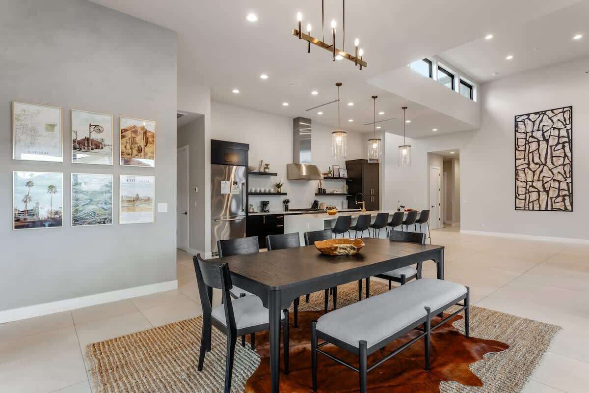 A modern dining area with a long table, chairs, and a chandelier.