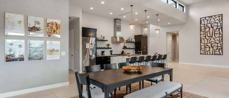 A modern dining area with a long table, chairs, and a chandelier.