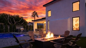 A modern outdoor patio with a fire pit, lounge chairs, and a pool.