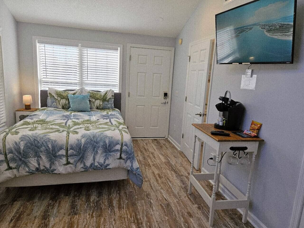 A bedroom with a bed, a desk with a chair, a television, and a door.