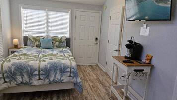 A bedroom with a bed, a desk with a chair, a television, and a door.