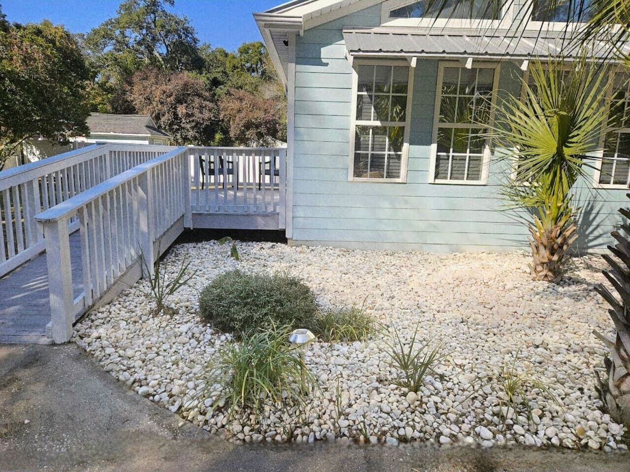 A house with a white deck, a small garden with gravel and plants, and a palm tree.