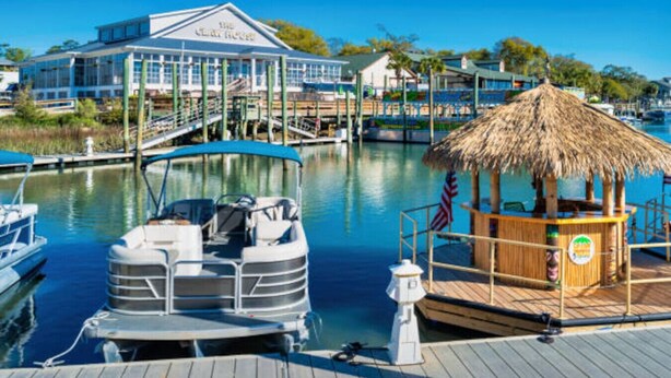 A marina with boats, a thatched-roof structure, and a building with a sign. - Drift Away with Inlet Vibes in Murrells Inlet at a Peaceful Studio (Murrells Inlet)