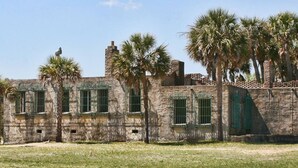 A stone building with multiple windows, some with green shutters, and palm trees in the foreground. - Drift Away with Inlet Vibes in Murrells Inlet at a Peaceful Studio (Murrells Inlet)