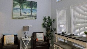 A room with a ceiling fan, a desk with a chair, a painting of a beach, and a window with blinds. - Drift Away with Inlet Vibes in Murrells Inlet at a Peaceful Studio (Murrells Inlet)