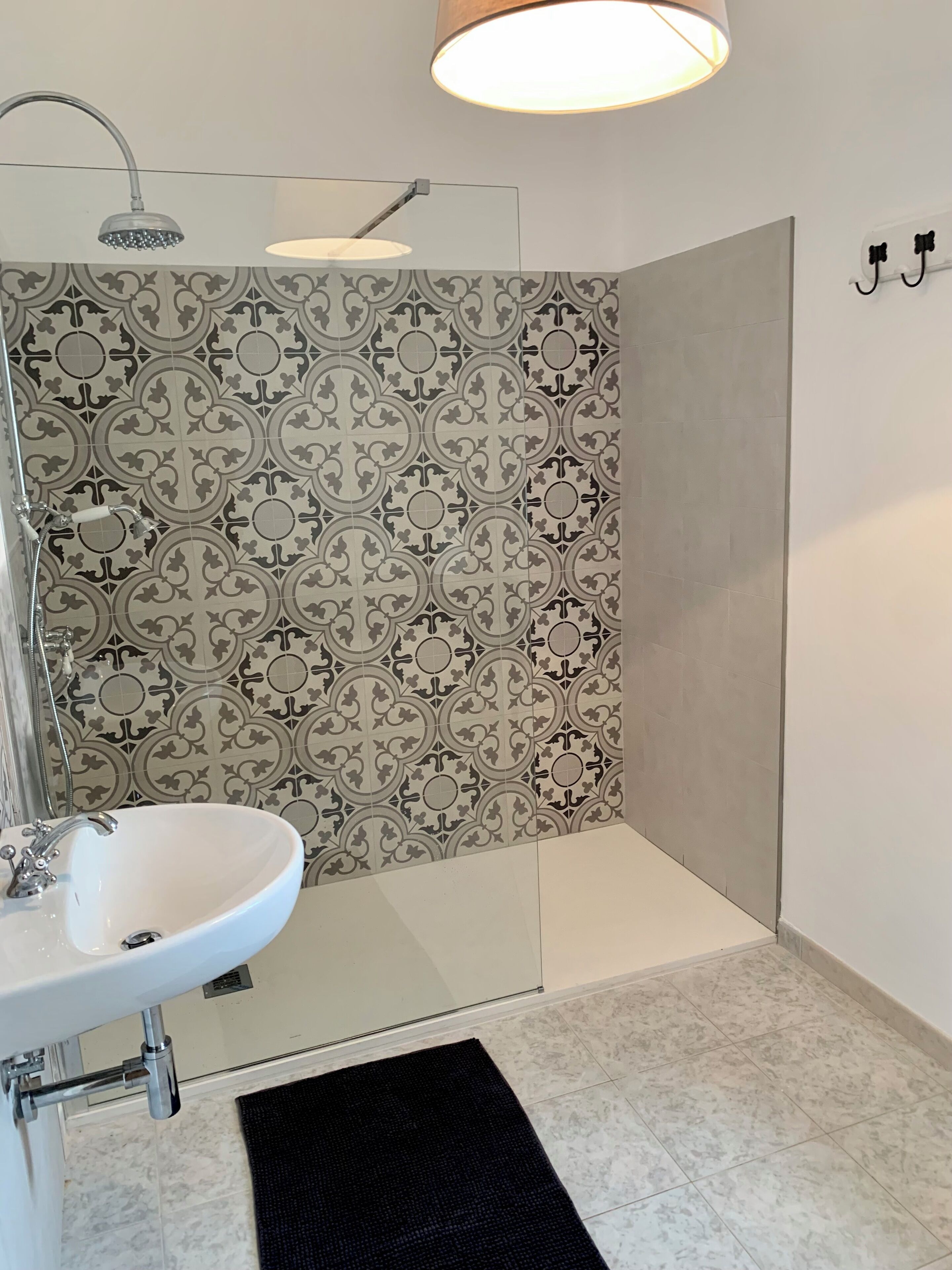 A bathroom with a white sink, a shower with a curved showerhead, and patterned tiles on the walls.