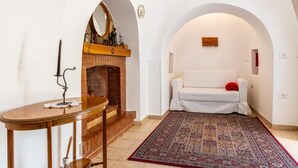Een kamer met een open haard, een witte bank en een kamerkleed met een patroon.