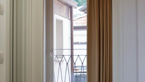 Habitació amb un llit, una porta corredissa de vidre que dona a una zona exterior amb barana metàl·lica, i una cortina en part desplegada.