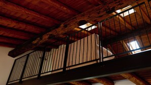 Un balcó de fusta amb barana metàl·lica, bigues a la vista i vista a l'espai interior inferior.