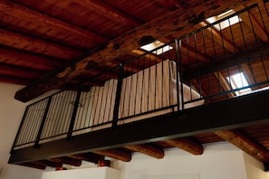 Un balcon en bois doté d’une rambarde en métal, de poutres apparentes et offrant une vue sur l’espace intérieur situé en contrebas.