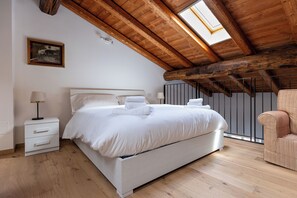 A bedroom with a wooden ceiling, a bed, a nightstand, a chair, and a window.