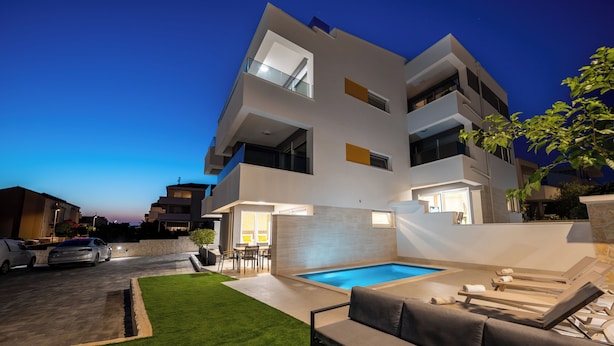 A modern multi-story building with a swimming pool, outdoor seating, and a well-maintained lawn. - Relax apartment with private pool I (Novalja)