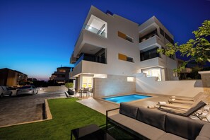 A modern multi-story building with a swimming pool, outdoor seating, and a well-maintained lawn. - Relax apartment with private pool I (Novalja)