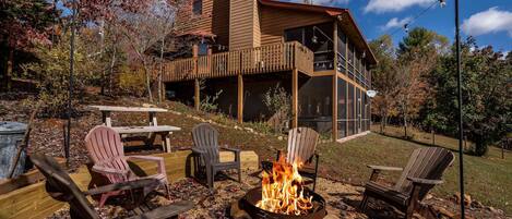 A wooden cabin with a deck, a fire pit, and outdoor seating.