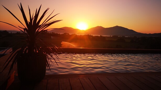 A sunset over a body of water with mountains in the background and a potted plant on a wooden deck.