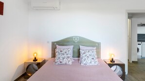A bedroom with a bed, two bedside lamps, an air conditioner, and a visible laundry area.