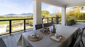 A dining area with a table set for two, a coffee pot, and a basket of pastries.
