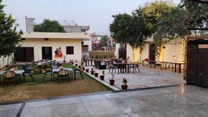 An outdoor seating area with tables and chairs, surrounded by potted plants and a small lawn. - Jai Hari Vilas Jodhpur (Jodhpur)