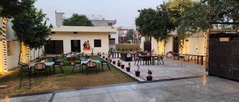 An outdoor seating area with tables and chairs, surrounded by potted plants and a small lawn.