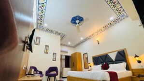 A hotel room with a large bed, a desk, two chairs, a small table, and a decorative ceiling. - Jai Hari Vilas Jodhpur (Jodhpur)