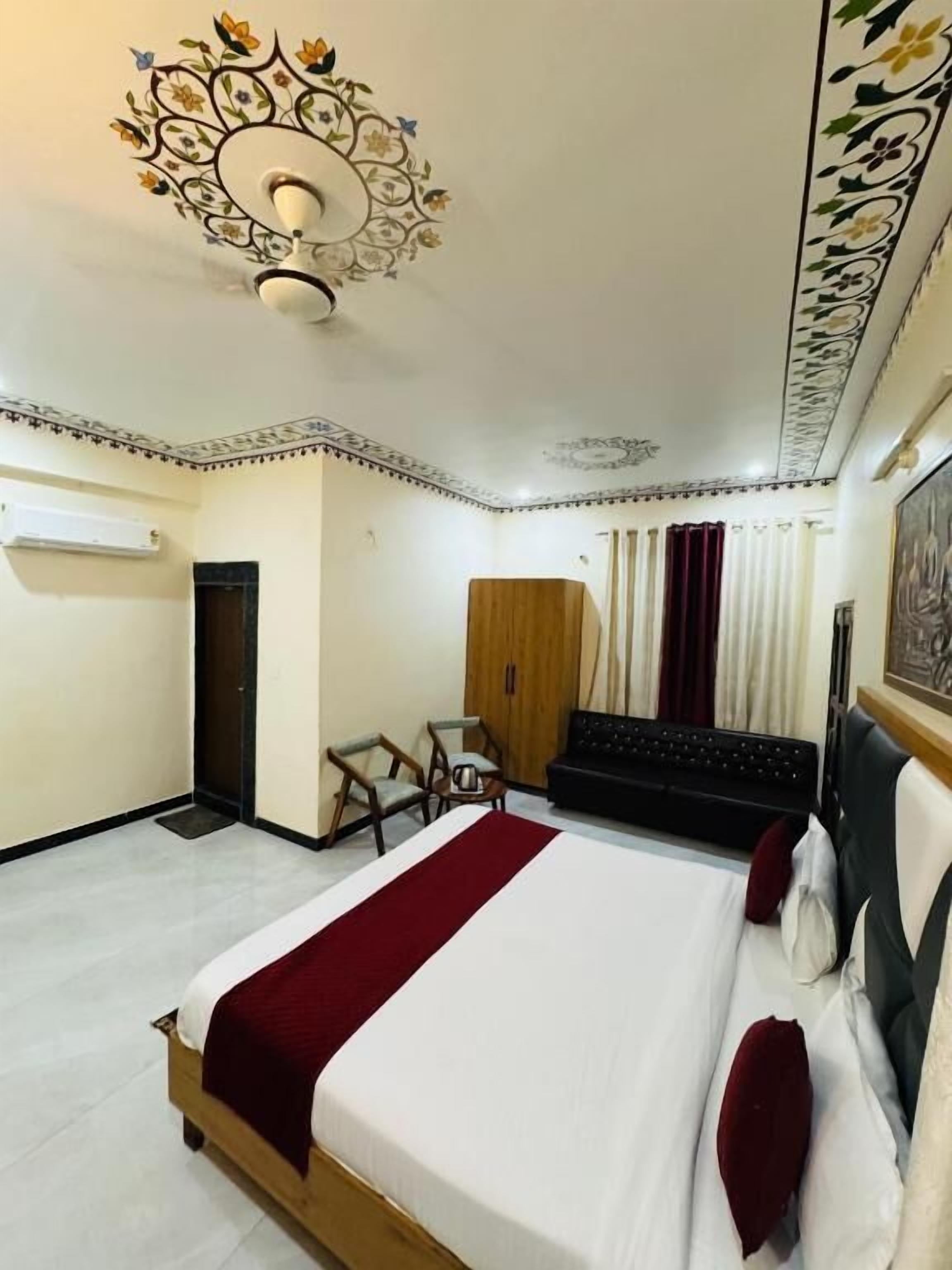 A hotel room with a large bed, a desk, a wardrobe, and a ceiling with floral patterns.