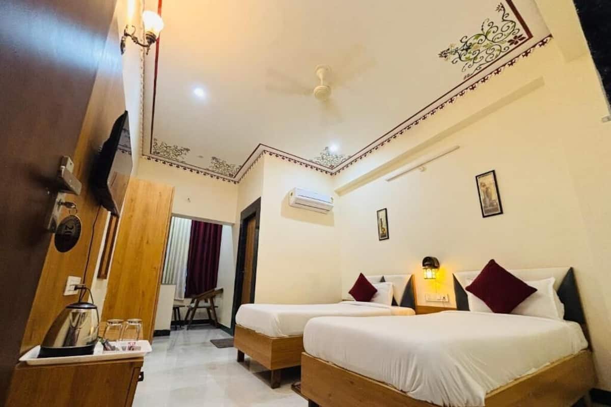 A hotel room with two wooden beds, a small desk with a kettle, and an air conditioning unit on the wall.