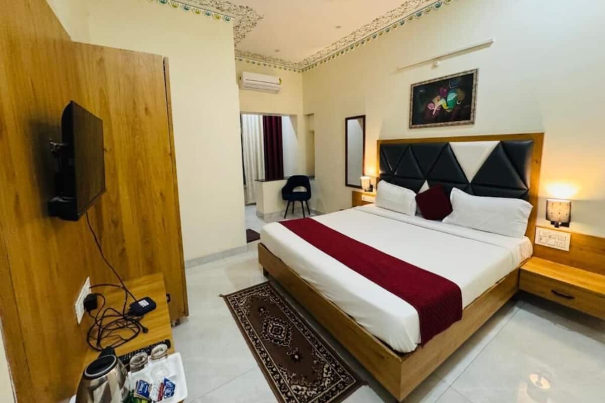 A hotel room with a large bed, a wooden wardrobe, a television, and a desk with a lamp.