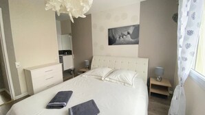A hotel room with a bed, bedside tables, a nightstand, a mirror, a painting on the wall, and a window with curtains.