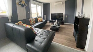 A modern living room with a black leather sofa, a glass coffee table, a flat-screen TV, and a dark wooden cabinet.