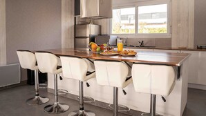 A modern kitchen with a central island, bar stools, stainless steel appliances, and a window providing natural light.