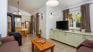 A cozy living room with a sofa, a wooden coffee table, a television, and a kitchen area with a stove and cabinets.