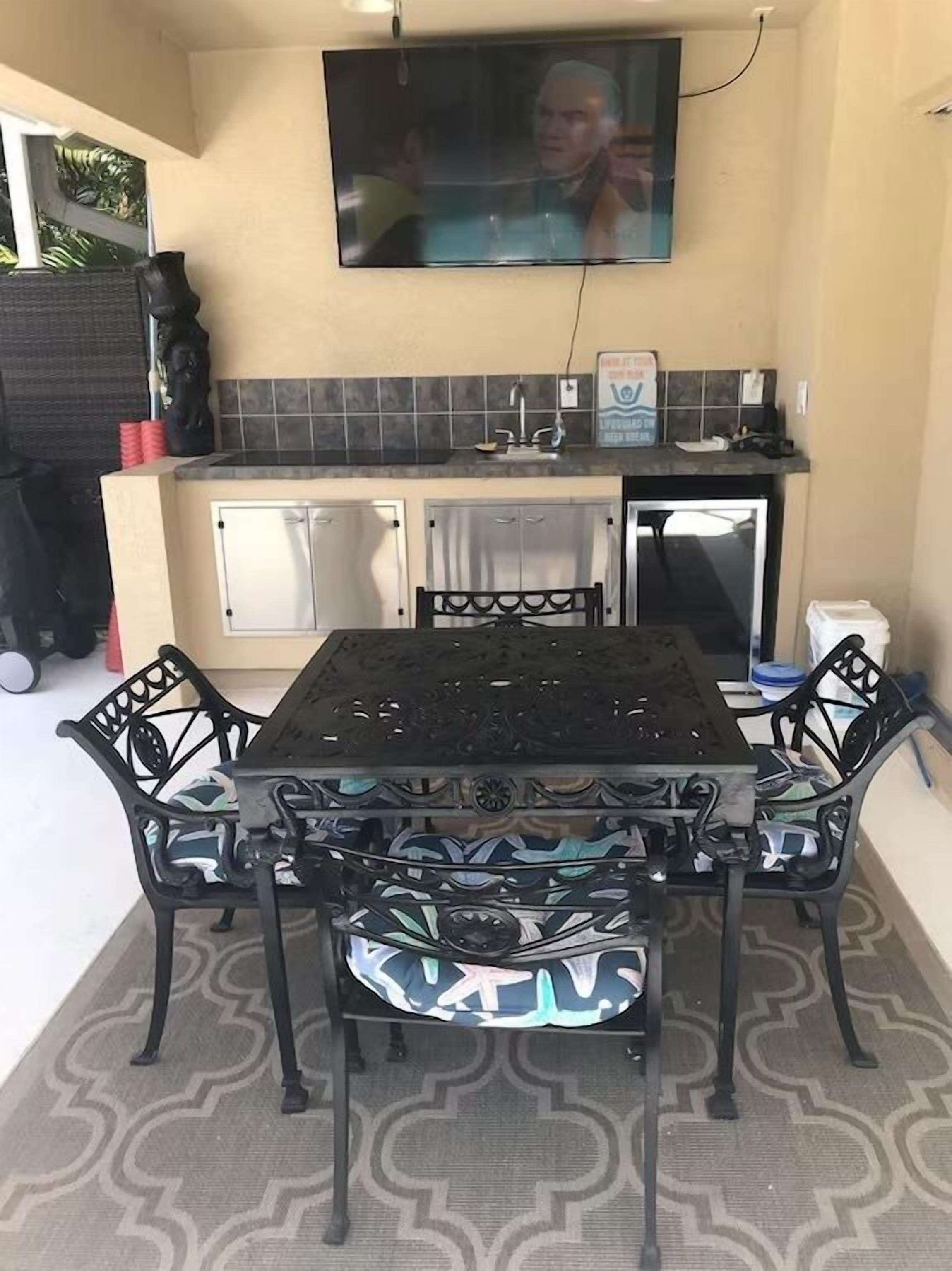 Un comedor con una mesa y sillas negras, un televisor montado en la pared y un salpicadero de azulejos.